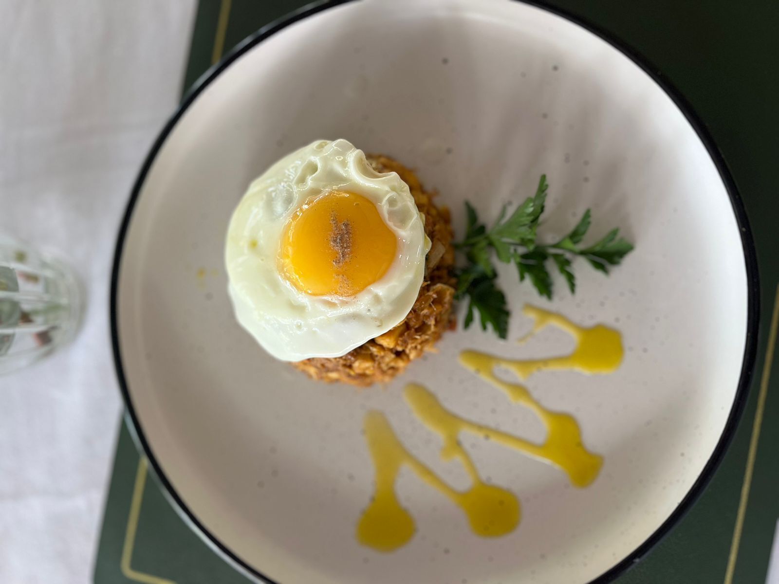 Un tazón con un huevo frito, perejil y salsa amarilla.