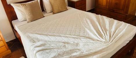 A neatly made bed with a quilted white bedspread, a wooden headboard, and two bedside tables with lamps.