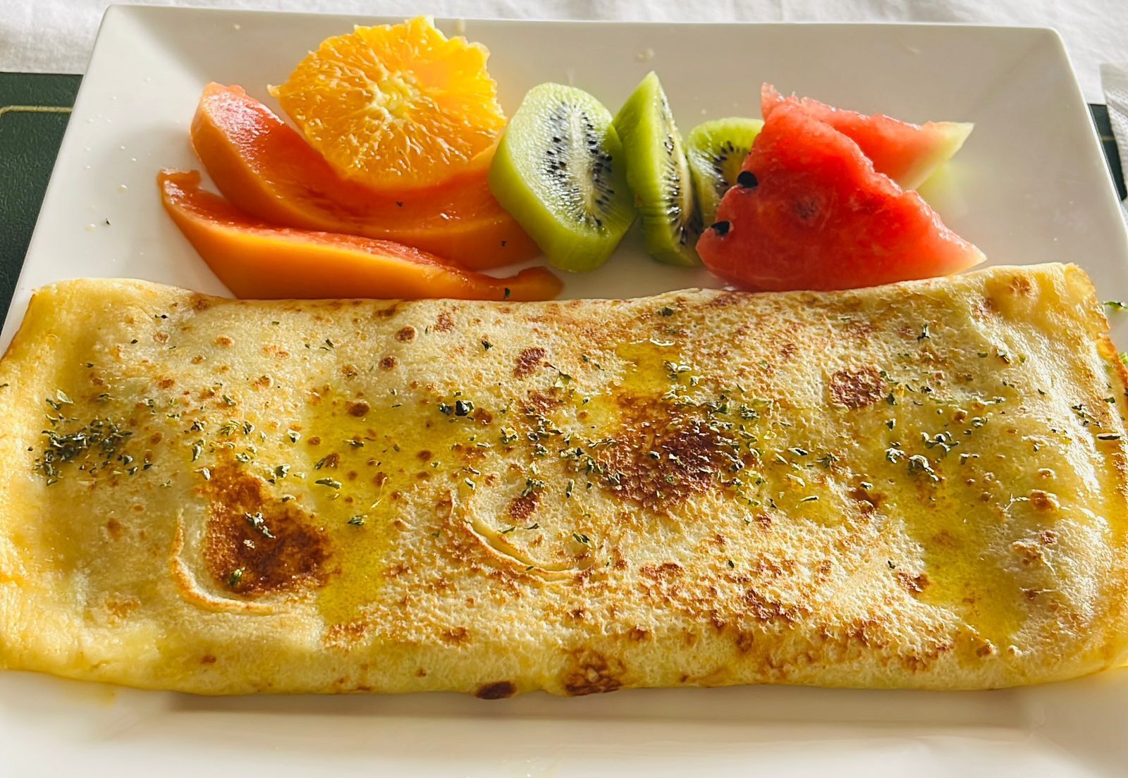 Une assiette avec une omelette pliée et des fruits coupés en tranches.
