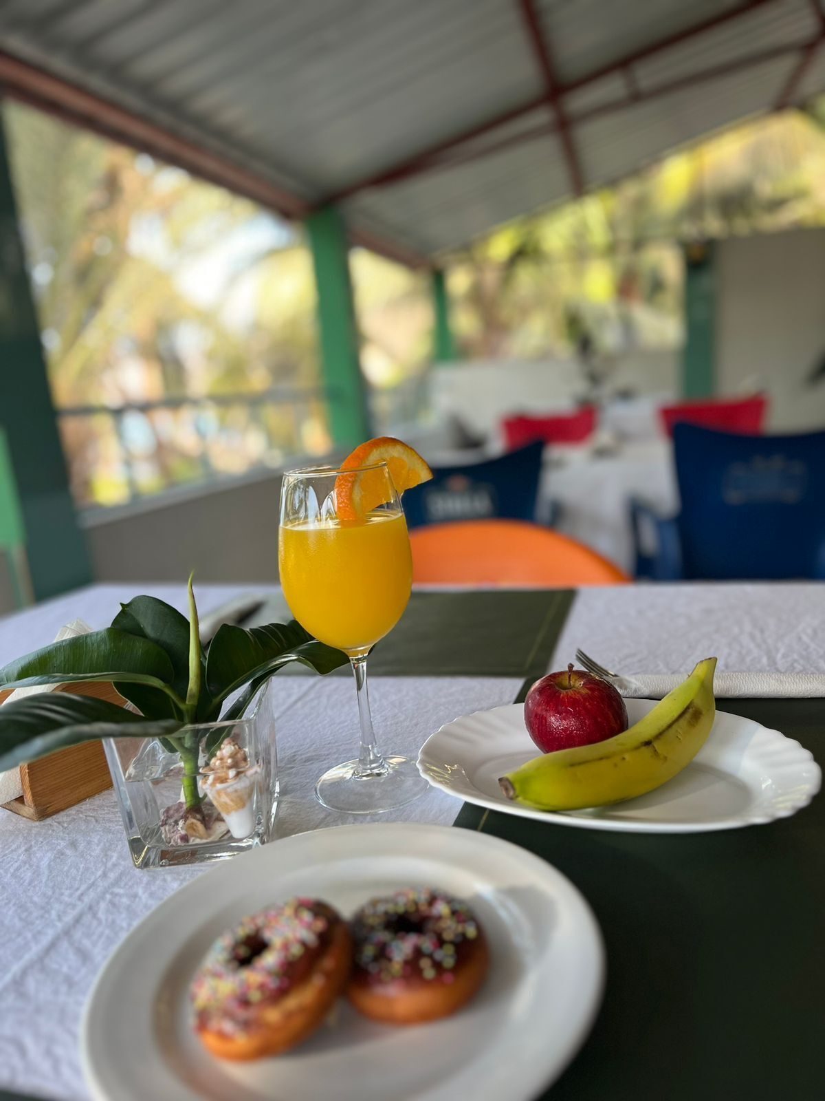 A table with a glass of orange juice, a plate with a banana and an apple, and two donuts.