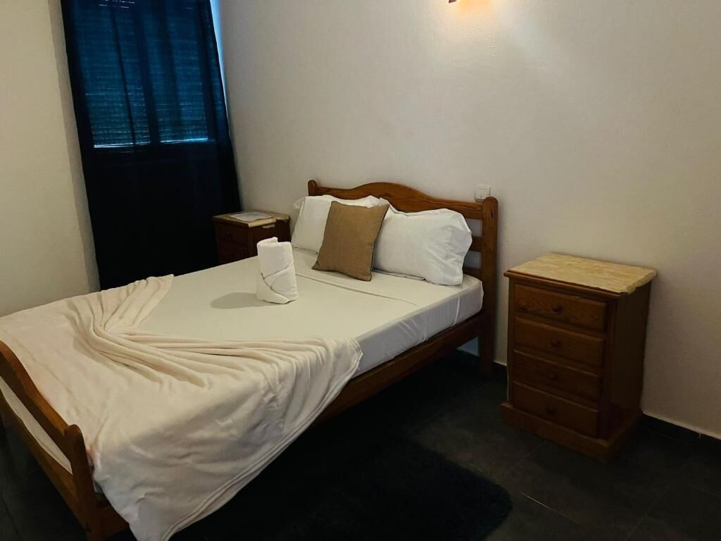 A neatly made bed with a white bedspread and pillows, a wooden headboard, a bedside table with a lamp, and a nightstand with a lamp.
