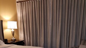 Ein Hotelzimmer mit einem großen Bett, einem Sessel, einer Lampe und einem Vorhang.