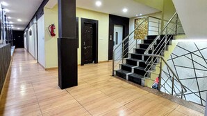 Un corridoio d'albergo con una scala e un estintore a muro.