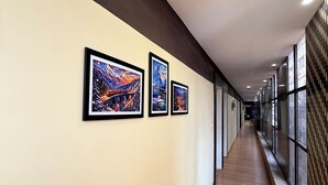 Un corridoio con opere d'arte incorniciate alle pareti, pavimento in legno e ampie finestre su un lato.