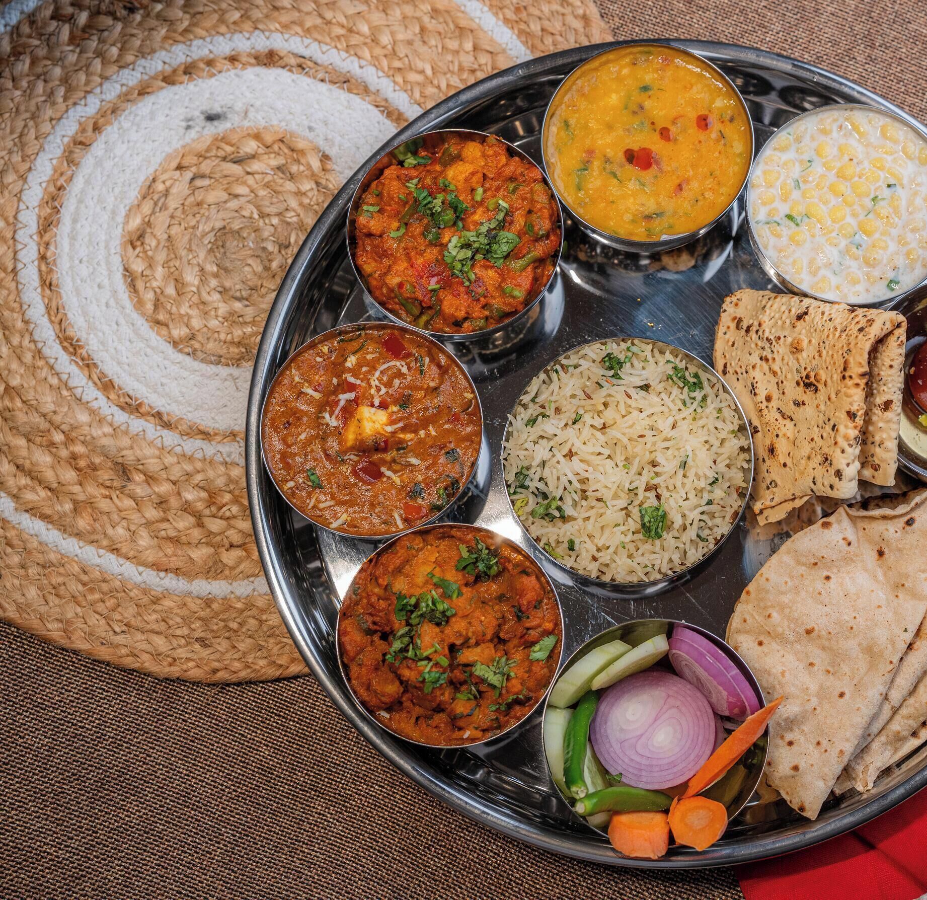 A traditional Indian meal with various dishes and flatbreads on a metal tray.