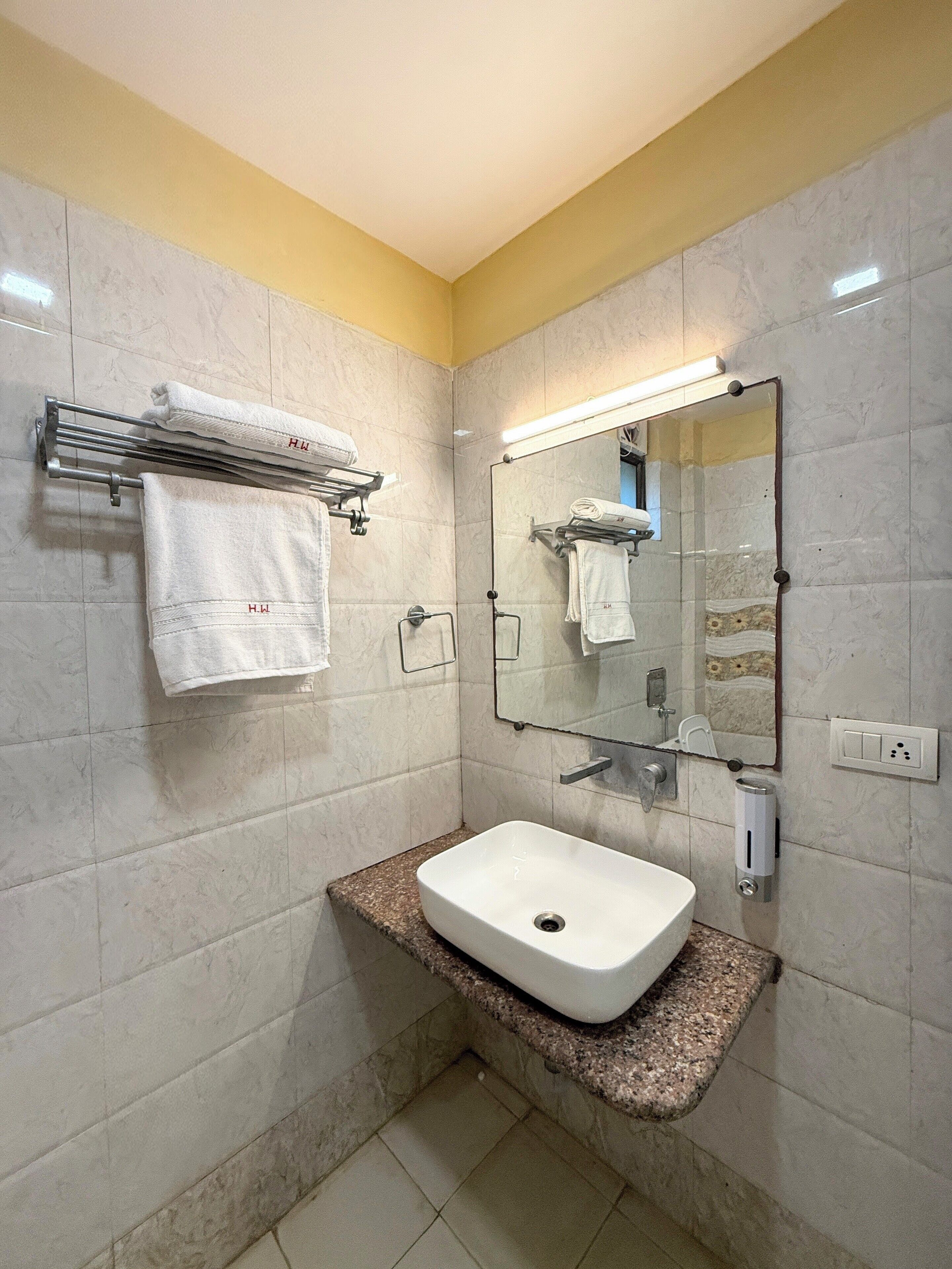 A bathroom with a white sink, marble walls, a towel rack, and a mirror.
