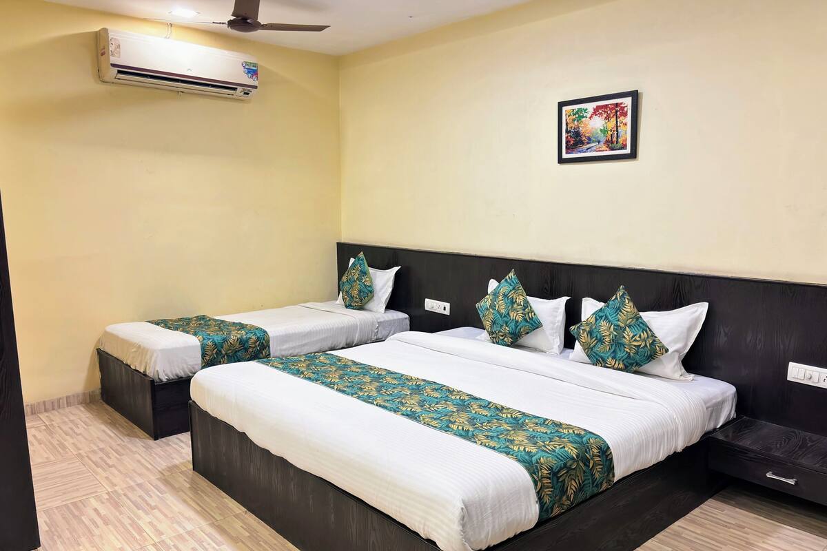A hotel room with two beds, a ceiling fan, an air conditioner, a wall-mounted painting, and a wooden floor.