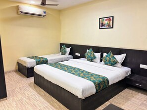 A hotel room with two beds, a ceiling fan, an air conditioner, a wall-mounted painting, and a wooden floor. - Hotel Wardhman (Jabalpur)