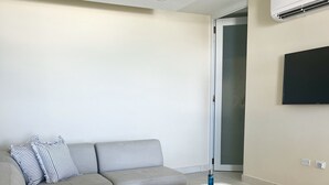 Un salon moderne avec un canapé d’angle gris, un petit pouf et un téléviseur à écran plat fixé au mur.