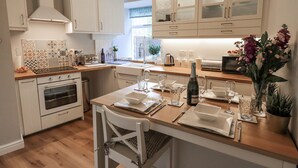A modern kitchen with white cabinetry, a wooden countertop, and a dining area set for six. - Olive Cottage (Kirkby Stephen)
