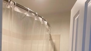 A bathroom with a shower curtain, a toilet, and a wall with a vertical tile pattern. - Arrowhead Inn (New Salem)