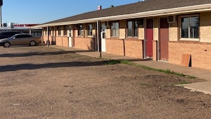 A motel with a row of rooms, a parking lot, and a building in the background. - Arrowhead Inn (New Salem)