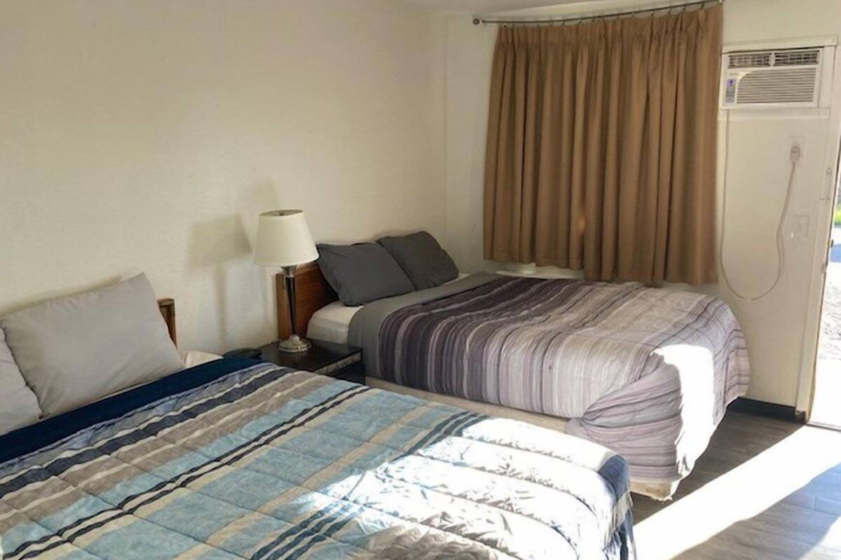 Un dormitorio con dos camas, una mesita de noche con lámpara y una ventana con cortinas.