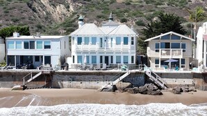 Ein Küstenhaus mit mehreren Etagen, einem Balkon und einer Treppe zum Strand.