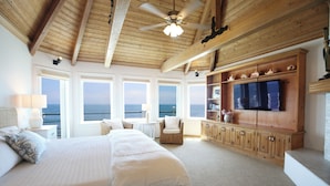 Ein geräumiges Schlafzimmer mit einem großen Bett, einem Fernseher, Holzschränken und Blick auf das Meer.