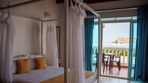 Un letto a baldacchino con tenda, due cuscini e vista su un balcone con tavolo e sedie.