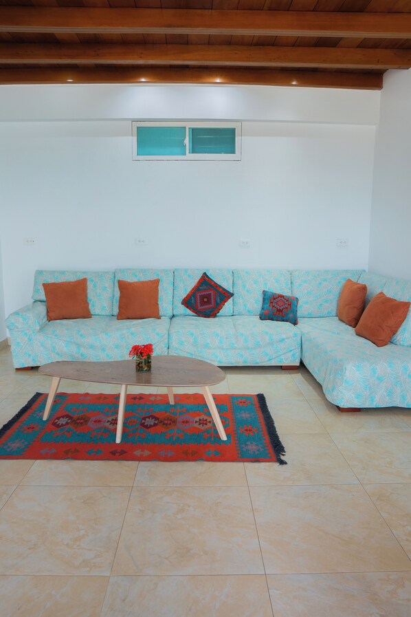 Un salon avec un canapé turquoise, des coussins marron, une table basse en bois et un tapis à motifs.