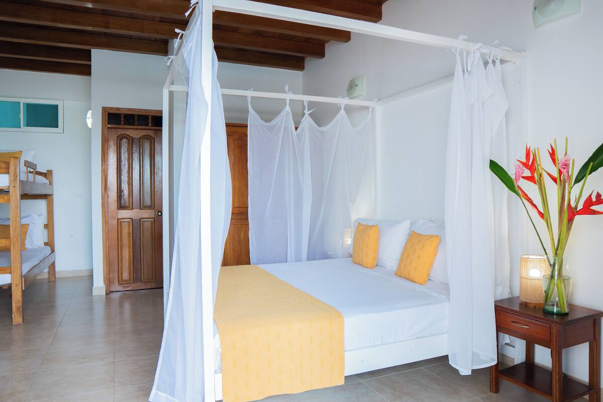 Una cama con dosel, una mesita de noche con lámpara y una silla de madera.