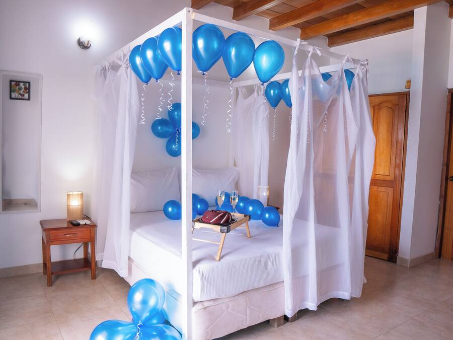 A four-poster bed with a canopy, blue balloons, and a tray with a handbag and champagne glasses.