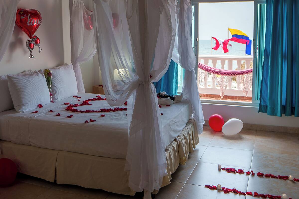 Un dormitorio con cama con dosel, ventilador de techo, balcón con vistas y cama decorada con pétalos de rosa.