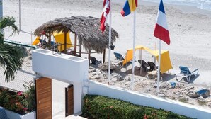 A beachside view with flags, a thatched-roof structure, and beach chairs. - Hotel 3 Banderas Manzanillo del Mar  (Cartagena)