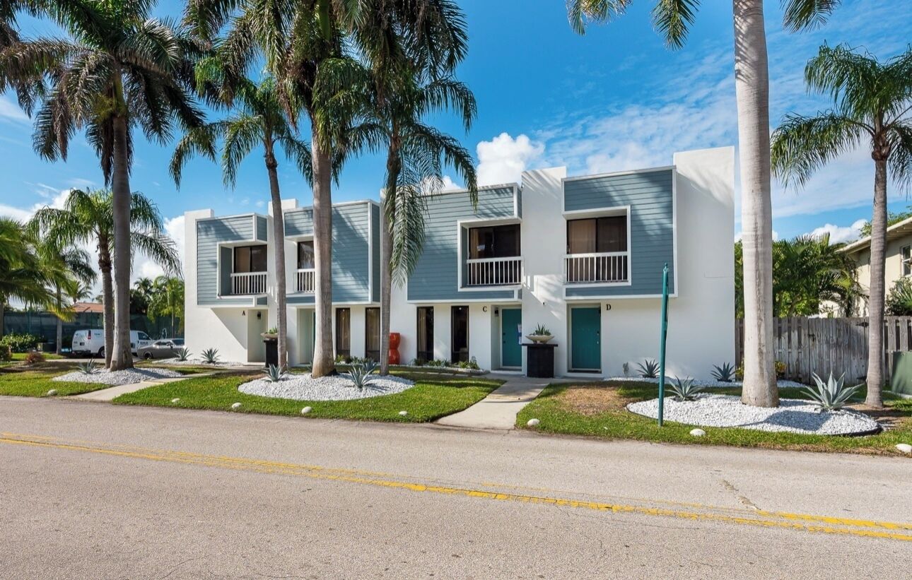 A modern multi-story residential building with a symmetrical facade, balconies, and a well-maintained lawn with palm trees.