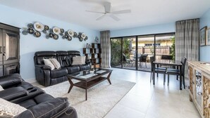 Ein geräumiges Wohnzimmer mit einer schwarzen Ledersofa, einem Glastisch und einem Essbereich mit Tisch und Stühlen.