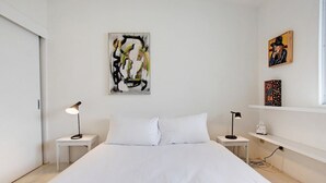 A minimalist bedroom with a large bed, two bedside tables with lamps, and artwork on the walls.