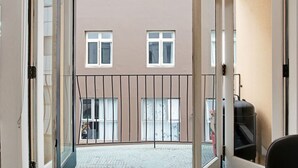 A view from a balcony with a glass door, overlooking a courtyard with a building in the background.