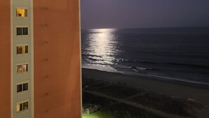Un immeuble de grande hauteur, doté de nombreuses fenêtres, qui offre une vue sur une plage où l’on peut apercevoir le reflet de la lune sur l’eau.