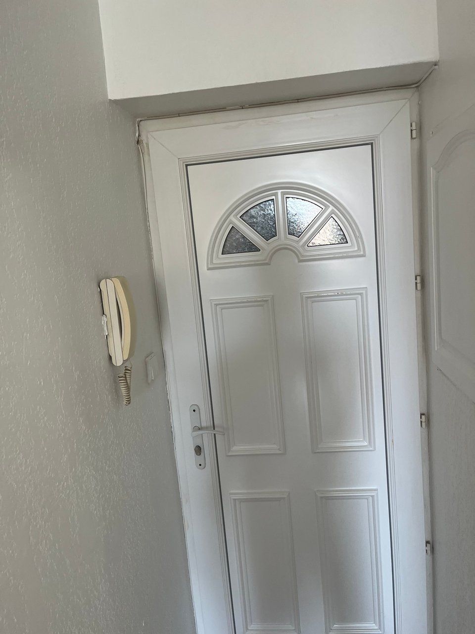 Una puerta blanca con un panel de vidrio y un teléfono instalado en la pared a la izquierda.