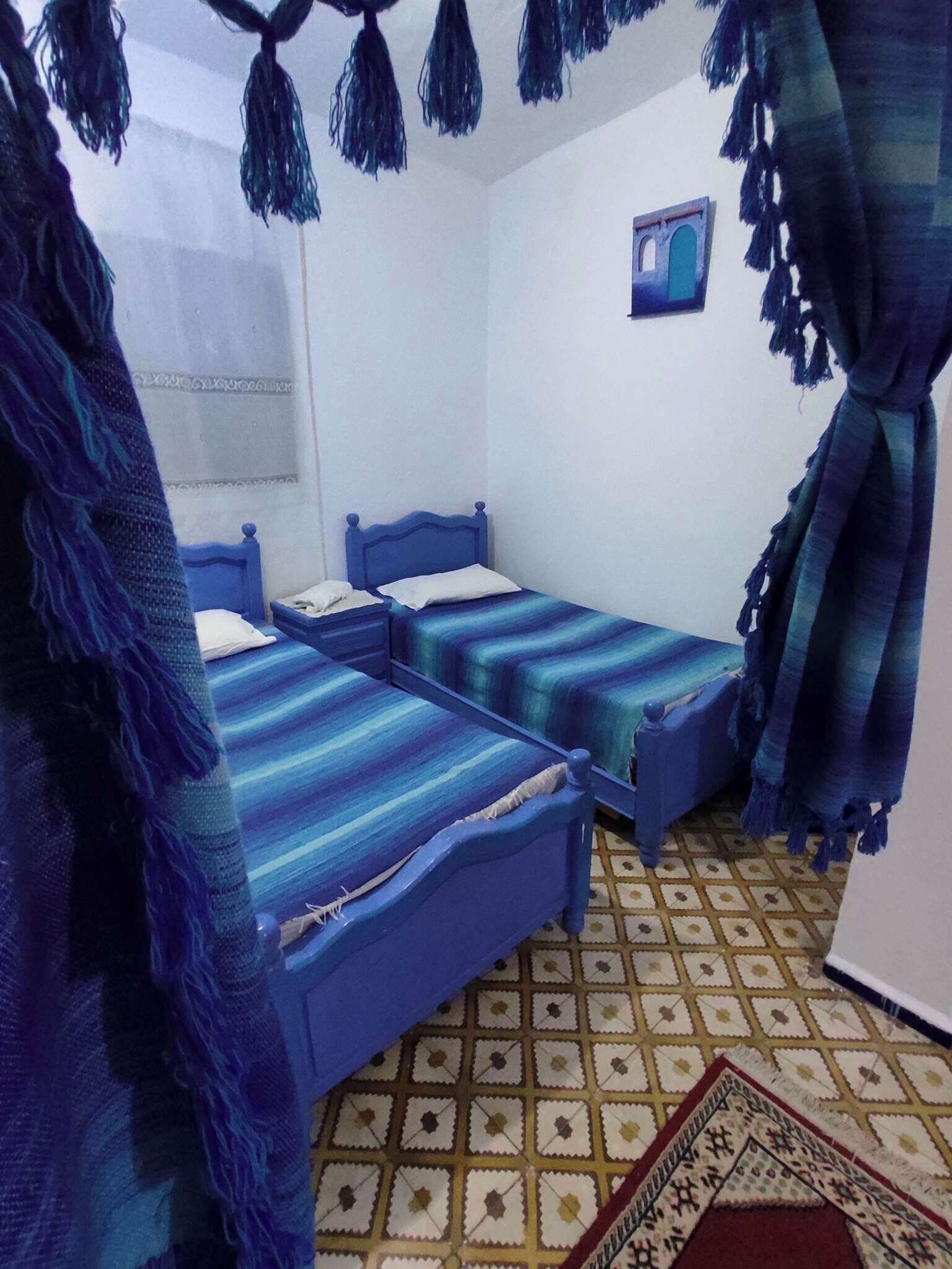 A room with three blue beds, a patterned floor, and a small wall-mounted picture.