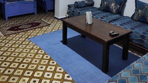 Een kamer met een patroon vloer, een zithoek, een bed met blauwe gordijnen en een schilderij aan de muur.