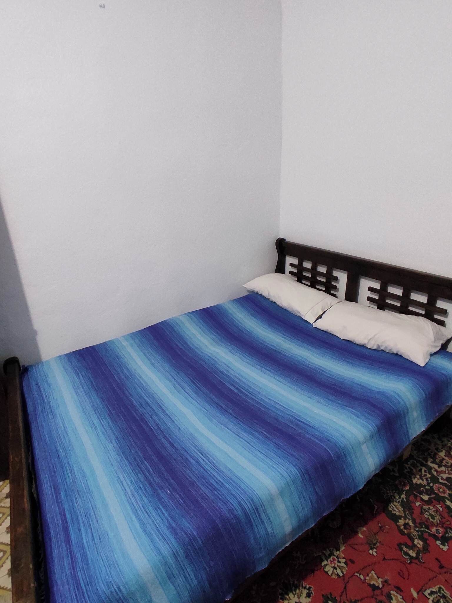 A single bed with a blue and white striped bedspread in a room with white walls and a wooden headboard.