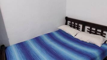 A single bed with a blue and white striped bedspread in a room with white walls and a wooden headboard.