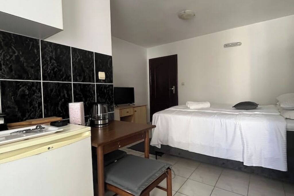 Een hotelkamer met een bed, een bureau met stoel, een kleine kitchenette en een donkere deur.