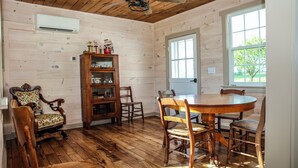 Una habitación con paneles de madera, una mesa redonda de madera y sillas, una estantería y una puerta que da al exterior.