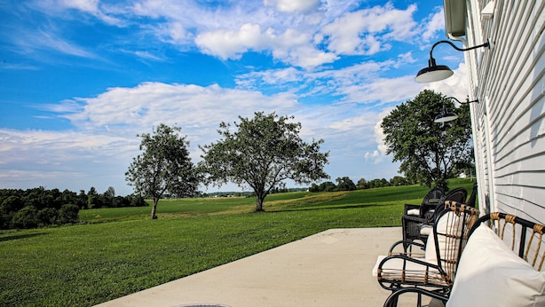 Un patio con muebles de exterior, una lámpara y vistas a un campo cubierto de césped y árboles.