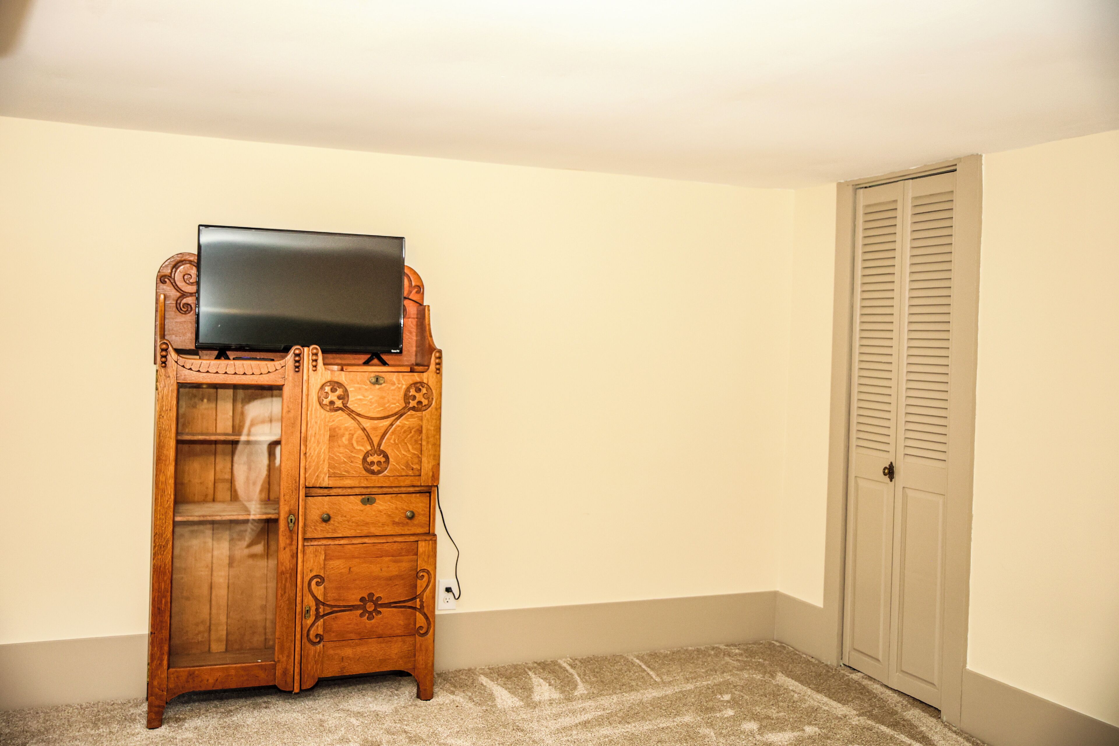 Un aparador de madera con un televisor de pantalla plana encima, un mueble con puerta de vidrio y una puerta con contraventanas.