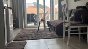 Un salon comprenant un canapé, une petite table et un fauteuil. Une porte-fenêtre coulissante donne accès à un espace extérieur.