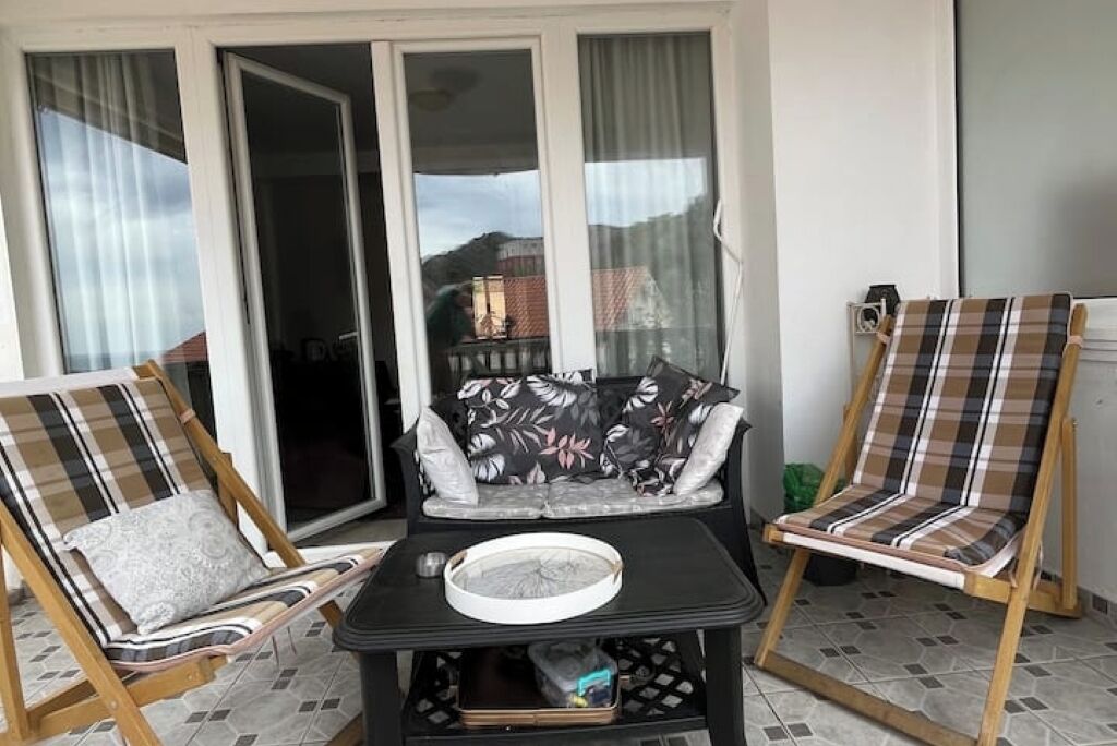 A balcony with two wooden lounge chairs, a black table, and a sofa with floral cushions.