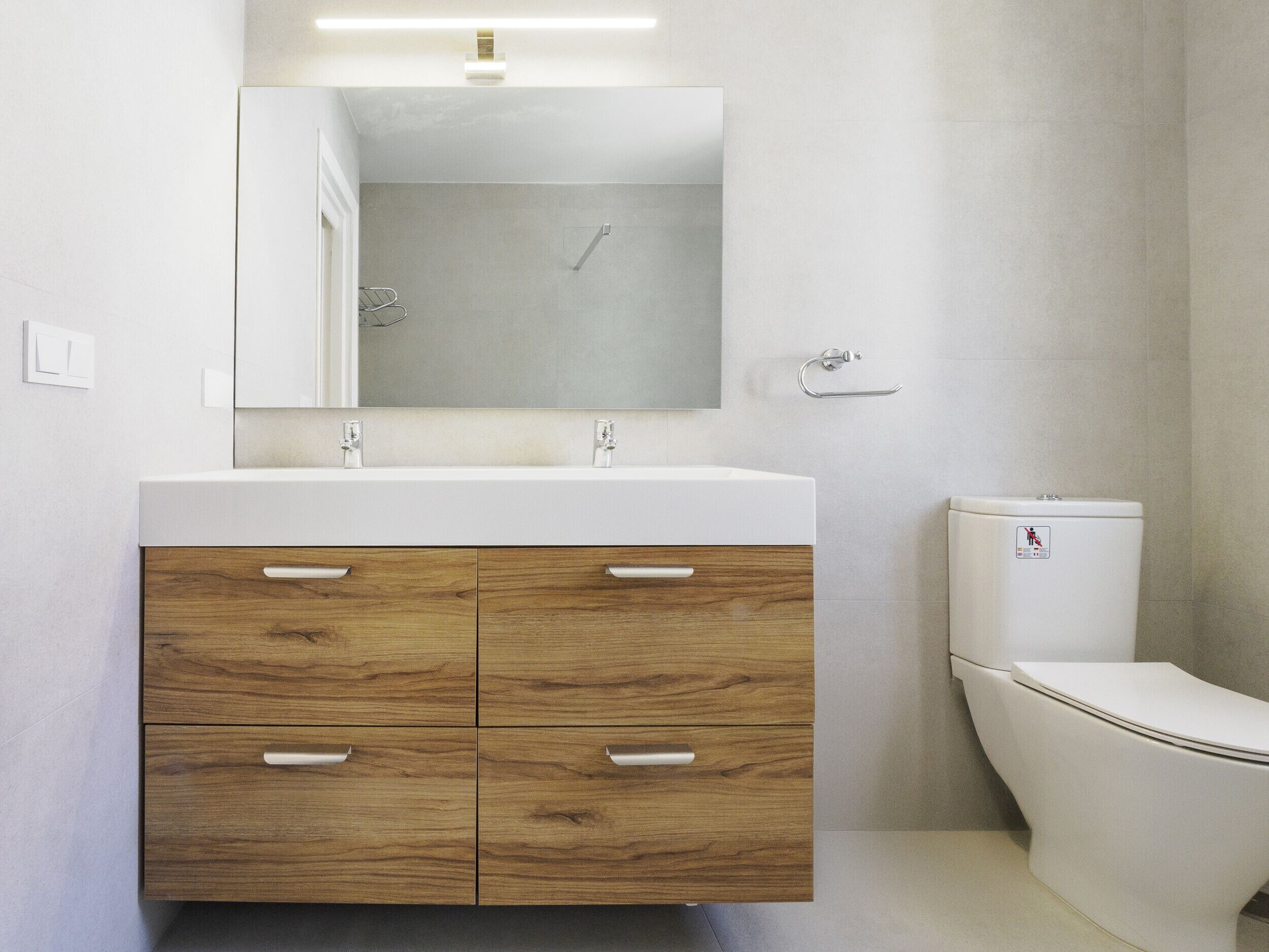 Ein modernes Badezimmer mit einem Holzbadschränke, einem großen Spiegel und einer Toilette.
