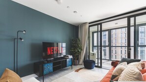 A modern living room with a large TV, a sofa, and a large window with a city view.