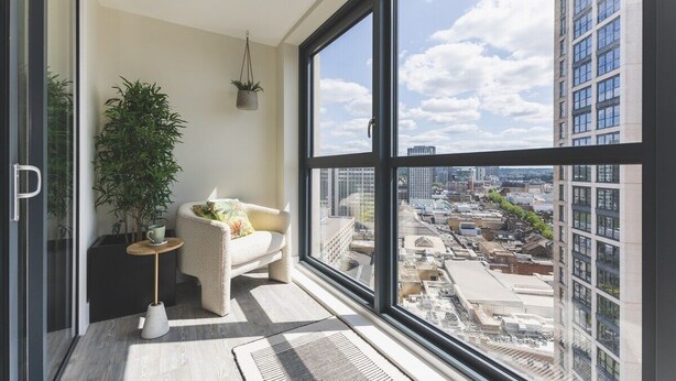 A modern apartment with a large window, a potted plant, a small round table, and a comfortable chair.