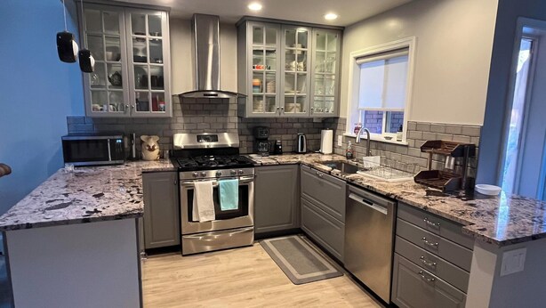 A modern kitchen with stainless steel appliances, grey cabinetry, and a wooden floor.