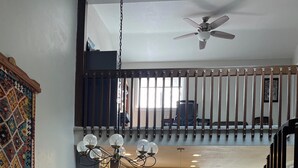A spacious dining area with a high ceiling, a staircase, and a kitchen in the background.
