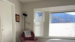 A bedroom with a bed, a chair, a window with blinds, and a door.