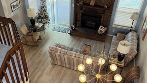 A spacious living room with a fireplace, a dining area with a wooden table and chairs, and a large window providing natural light.