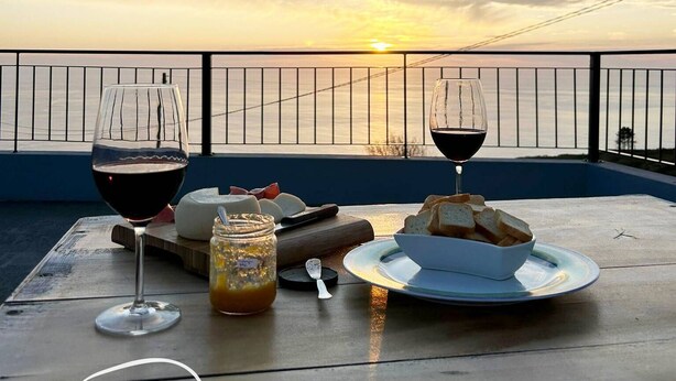 Ein Tisch mit Weingläsern, Käse, Brot und einer Marmeladenglas auf einem Balkon mit Blick auf einen Sonnenuntergang.