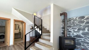 Eine Treppe führt zu einer zweiten Etage, eine Steinmauer und ein Kaminofen sind zu sehen.